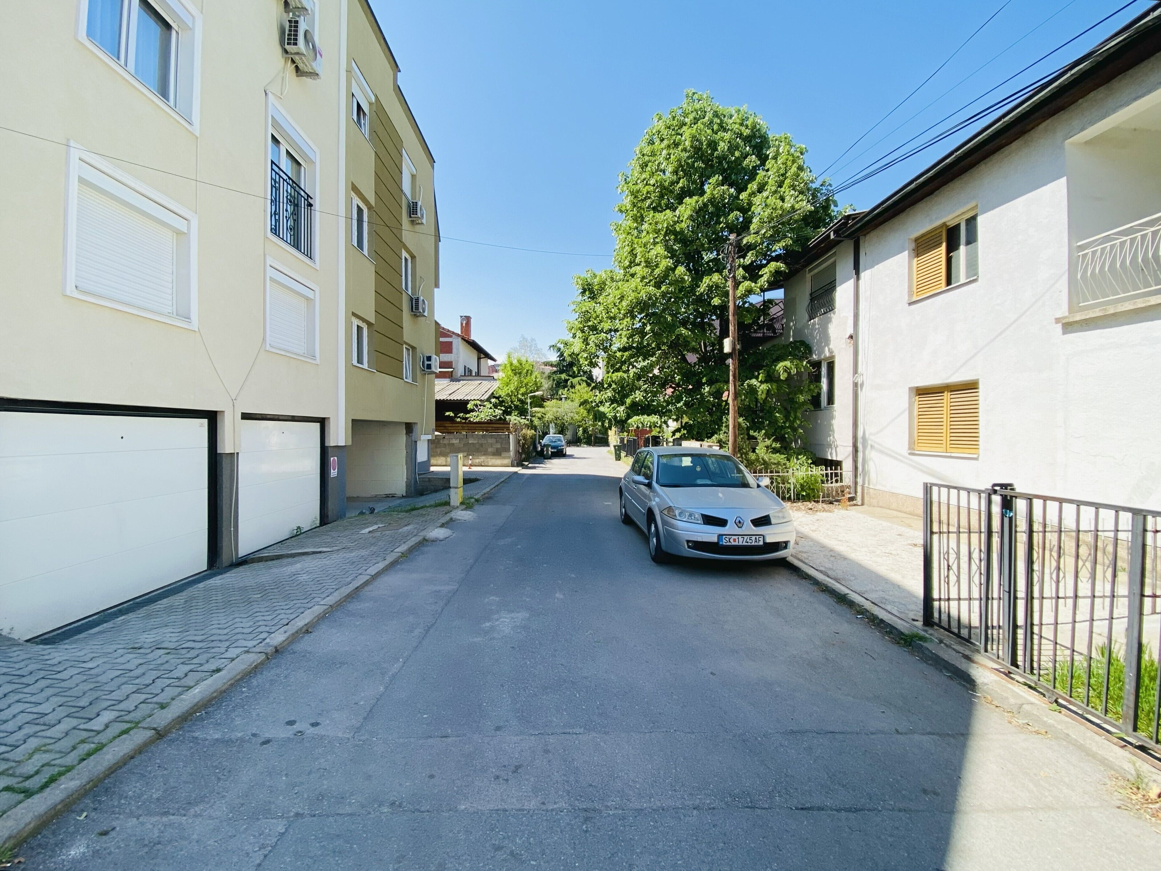 Een woonstraat met een geparkeerde auto, gebouwen met balkons en een boom.