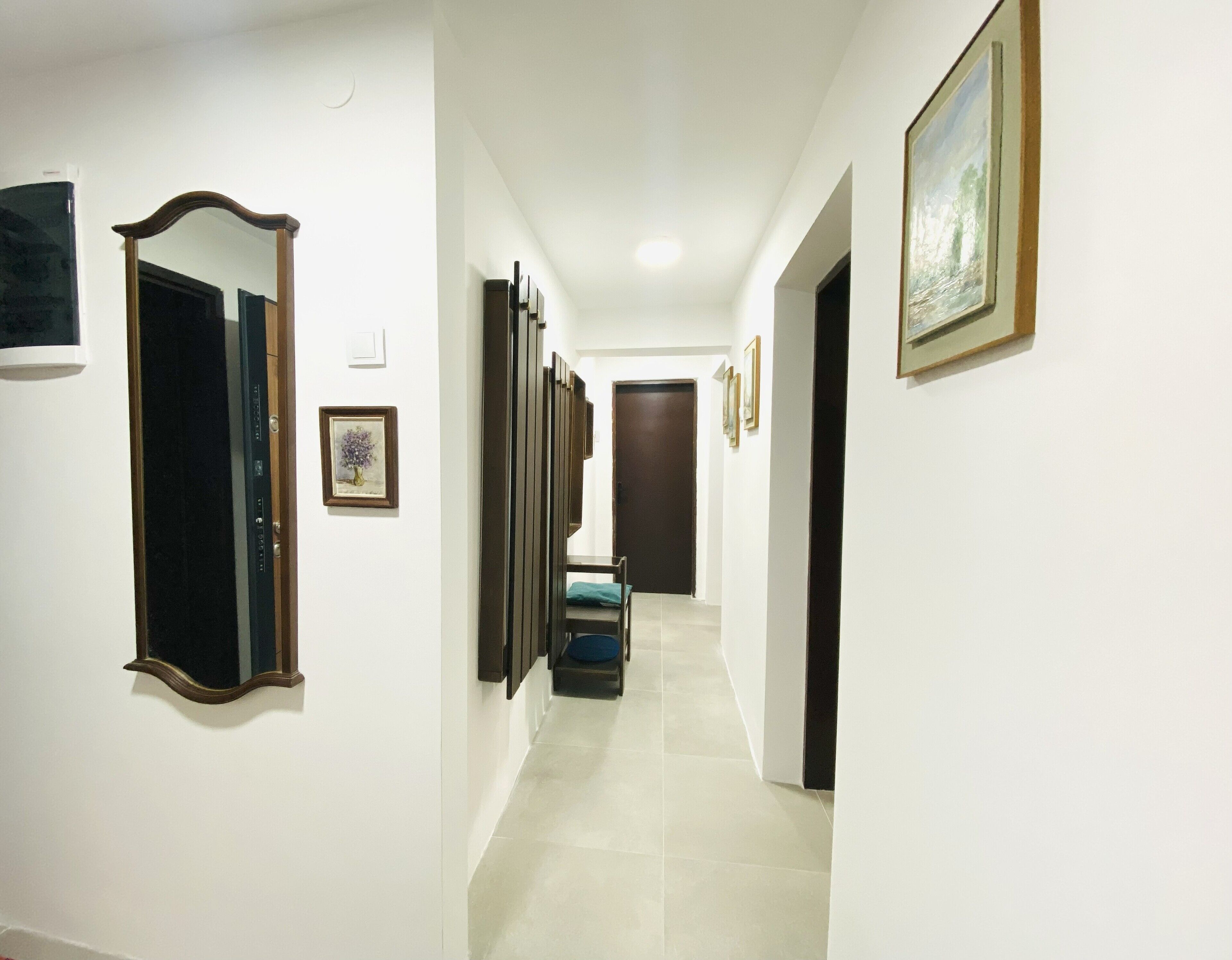 A hallway with a door at the end, a framed picture on the wall, and a blue chair in the center.