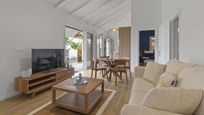 A spacious living room with a TV, wooden coffee table, beige sofa, and a dining area with chairs and a table. - Kaza 3 Anses - Two Bedroom Villa, Sleeps 6 (Sainte-Anne)