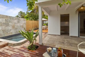 A modern outdoor patio with a hot tub, wooden deck, and a dining area with a table and chairs.