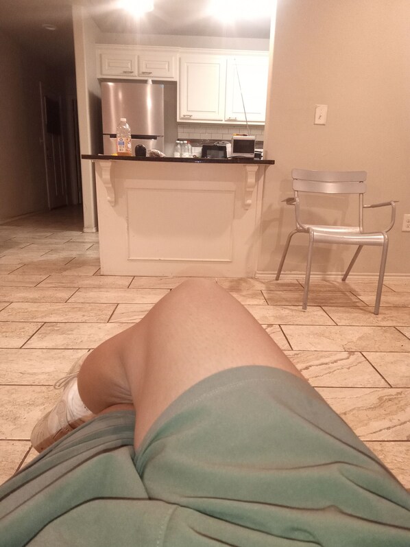 A room with a tiled floor, a kitchen area with cabinets and appliances, and a chair.