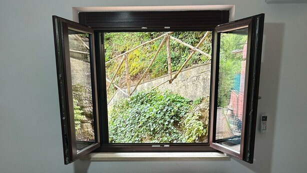 A room with a bed, a window with an open view of greenery, and a wall-mounted air conditioner. - Accommodation you love (Molinaccio)