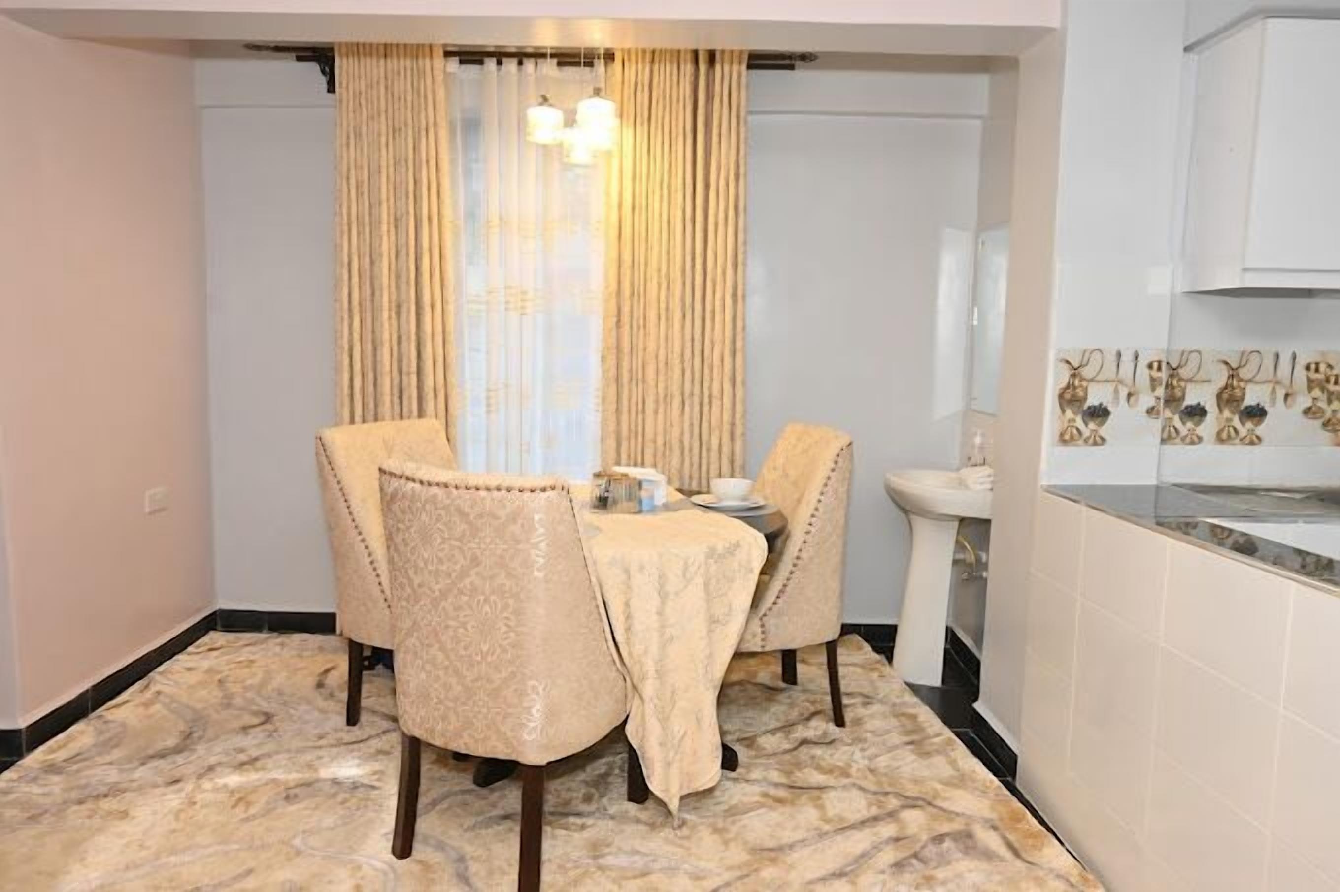A dining area with a table set for two, two chairs, a chandelier, and a sink with decorative tiles.