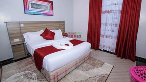 Un lit bien fait, recouvert d’une couvre-lit rouge et blanche, avec une tête de lit en bois et un tableau encadré accroché au mur.