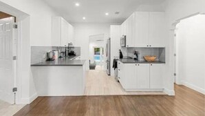 Una cucina moderna con mobili bianchi, un piano di lavoro scuro e un pavimento in legno.