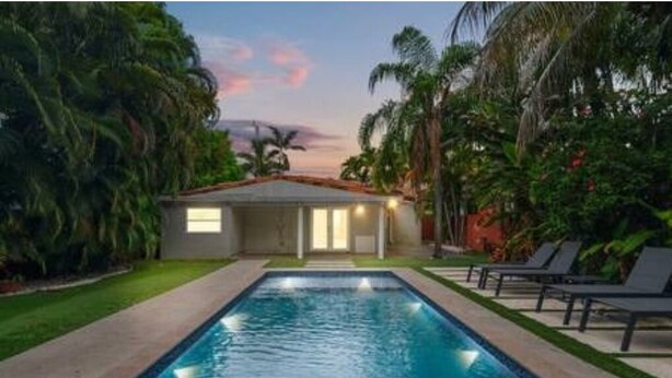 Una piscina con una casa sullo sfondo, immersa nel verde.