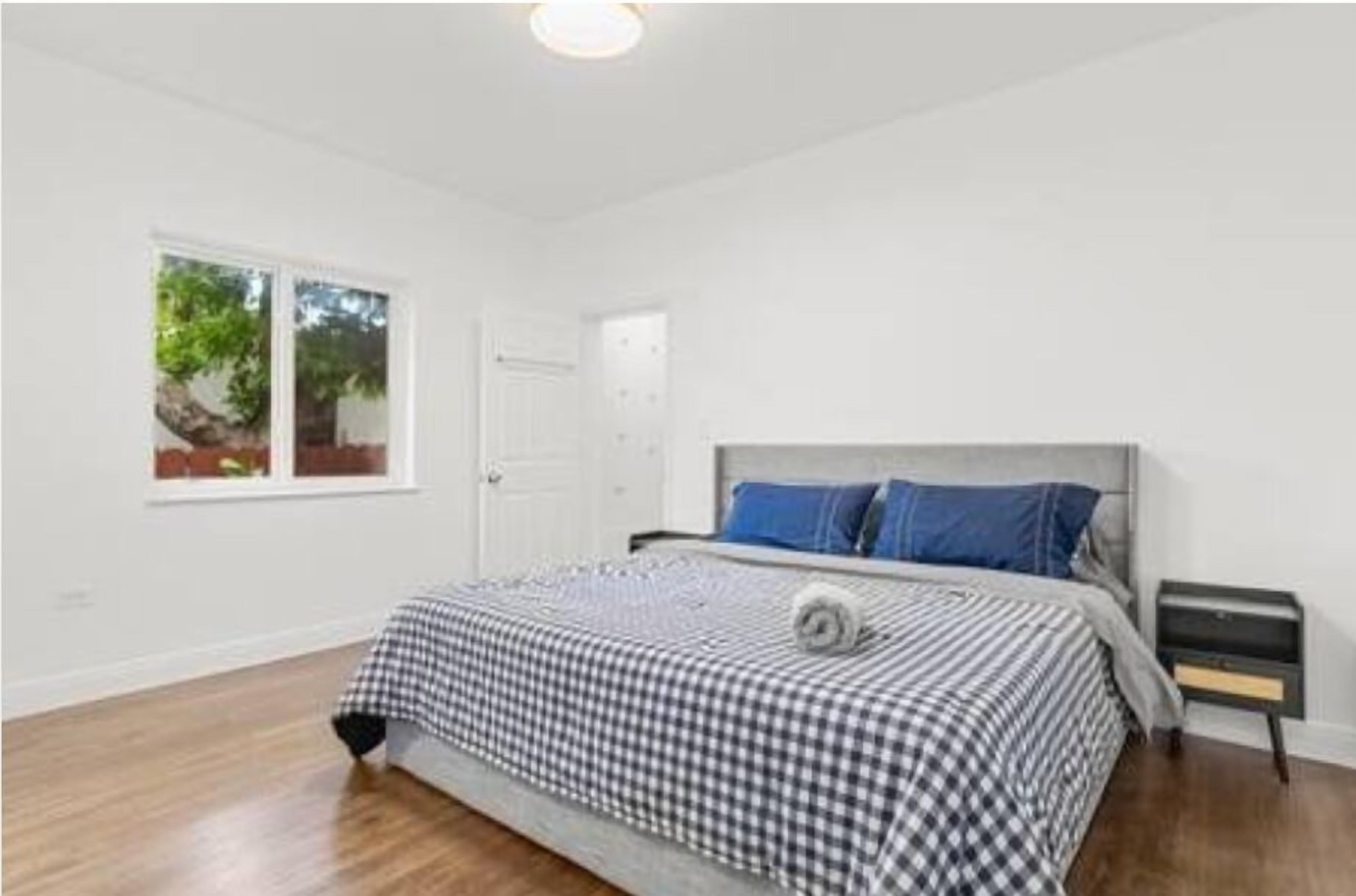 Un dormitorio con cama, mesita de noche, ventana y puerta.
