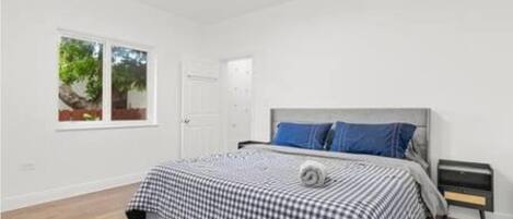 Un dormitorio con cama, mesita de noche, ventana y puerta.