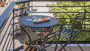 Una mesa con un plato de sushi y dos copas de vino en un balcón con barandas de metal y plantas en macetas.