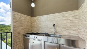 A modern kitchen with a stainless steel stove, sink, and cabinets, a hanging light fixture, and a balcony with a view of greenery. - Modern Home with Lush Mountain Views and Spectacular Shaded Terrace in Private Gated Community (Playa Potrero)