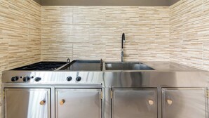 A kitchen with a stainless steel stove, sink, and cabinets, and a tiled backsplash. - Modern Home with Lush Mountain Views and Spectacular Shaded Terrace in Private Gated Community (Playa Potrero)