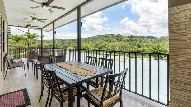 A balcony with a table and chairs, ceiling fans, and a view of a river and mountains. - Modern Home with Lush Mountain Views and Spectacular Shaded Terrace in Private Gated Community (Playa Potrero)