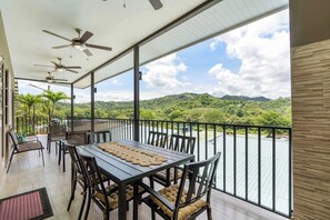 Un balcón con mesa y sillas, ventiladores de techo y vistas a un río y montañas.