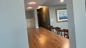 A spacious room with a long wooden table and chairs, recessed ceiling lights, and a framed picture on the wall.