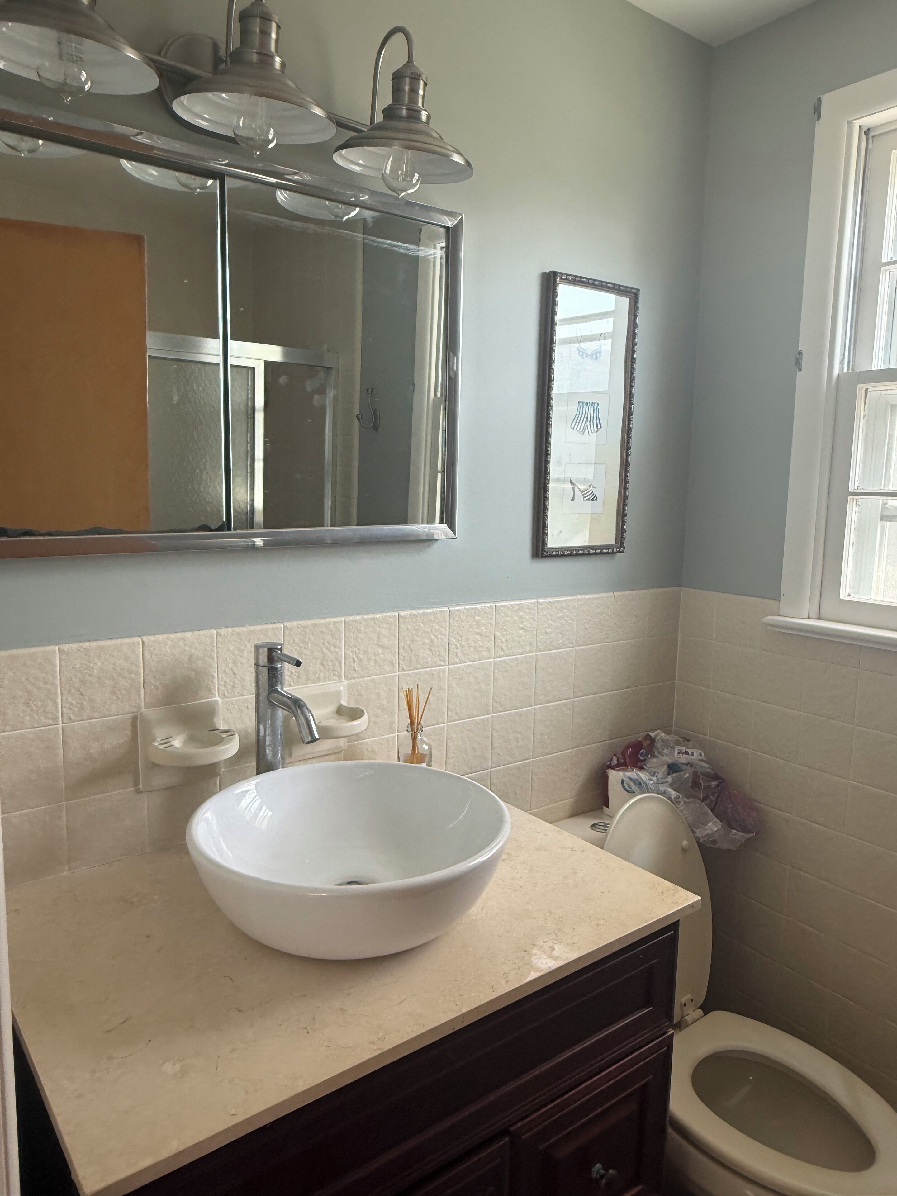 A bathroom with a white sink, a mirror, a toilet, and a window.