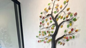Un comedor con mesa de madera, sillas blancas y una pieza de arte mural con motivos de árboles.