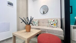 Un salón moderno con una mesa de madera, una silla roja, un sofá con cojines estampados, un espejo redondo y un florero con ramas negras.