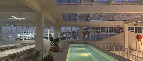 An indoor swimming pool with a view of the cityscape through large windows.