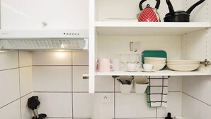 Una cocina con paredes de azulejos blancos, encimera blanca y estantes con utensilios de cocina.
