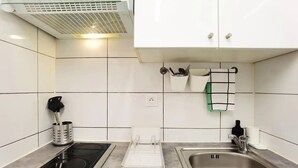Una cocina con azulejos blancos, estufa, pileta y un respiradero en el techo.