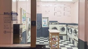 Una lavandería con varias lavadoras y secadoras, un piso a cuadros y carteles informativos en las paredes.