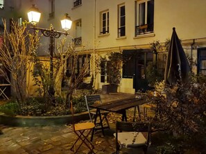 Un patio al aire libre con mesa y sillas de madera, rodeado de plantas y un farol.