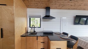 A modern kitchen with wooden cabinetry, a black countertop, and a built-in stove. There is a window with a view of trees and a door to the right. - The Northern Tickle. 20 minutes to Twillingate. Gorgeous views of the ocean. (Summerford)