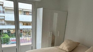 Un dormitorio con una cama grande, un ventanal corredero que da a un balcón y un armario blanco.