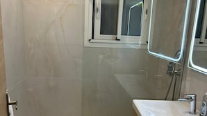 Un baño moderno con cabina de ducha de vidrio, tocador con espejo y un ventanal pequeño.