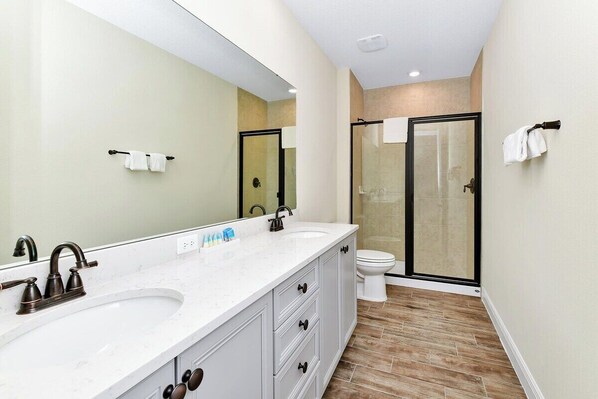 A modern bathroom with a double sink vanity, a large mirror, a toilet, and a glass-enclosed shower.