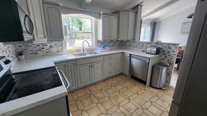 A kitchen with a tiled backsplash, stainless steel appliances, and a window with a view of greenery outside. - Relax in Comfort! (Cornwall)