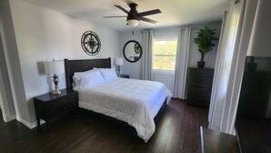 A bedroom with a bed, nightstands, a ceiling fan, a window with curtains, a potted plant, and a dresser. - Relax in Comfort! (Cornwall)
