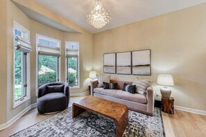 Una sala de estar con sofá, sillón, mesa de centro y una obra de arte en la pared.