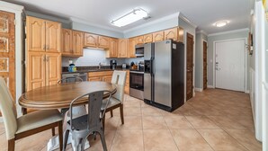 Una cocina con armarios de madera, un refrigerador de acero inoxidable, una mesa de comedor con sillas y piso de baldosas.
