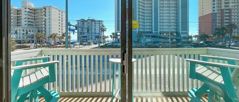 A balcony with turquoise chairs, a wooden floor, and a view of tall buildings and a street.