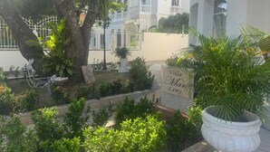 Une cour avec un grand arbre, une enseigne indiquant « Villa Ma Leny », et un bâtiment blanc en arrière-plan.