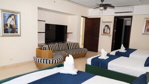 Une chambre d’hôtel avec trois lits, un canapé, une télévision et des œuvres d’art accrochées aux murs.