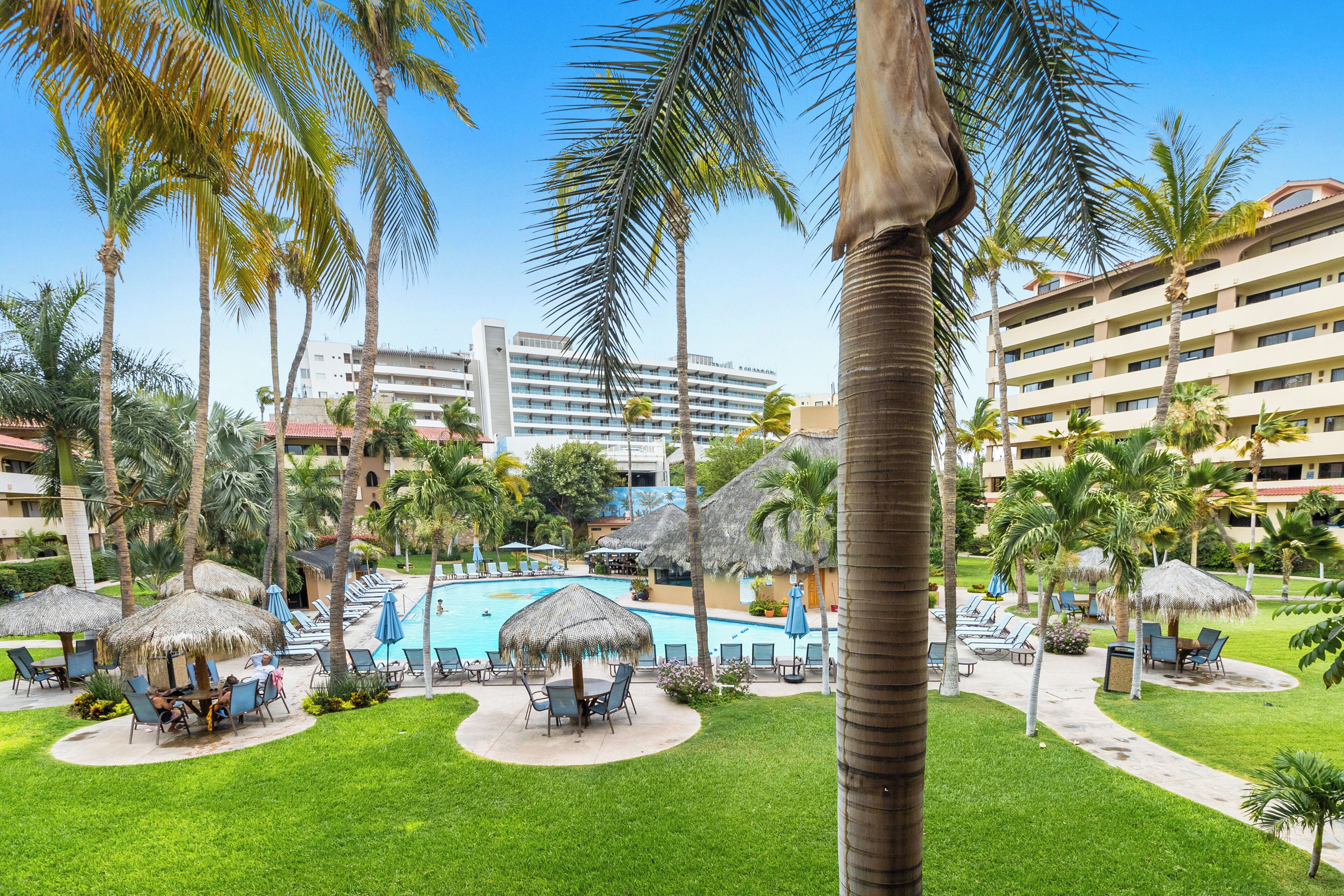 A resort with a swimming pool, palm trees, and lounge chairs.