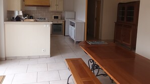 Kompakti keittiö, jossa on keskeinen saareke, ruokapöytä ja puinen kaappi.