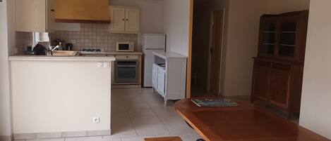 A compact kitchen with a central island, a dining table, and a wooden cabinet.