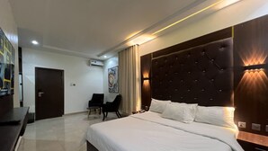 Ein Hotelzimmer mit einem großen Bett, einer dunkelbraunen Kopfteil und einer Sitzecke mit zwei Sesseln.