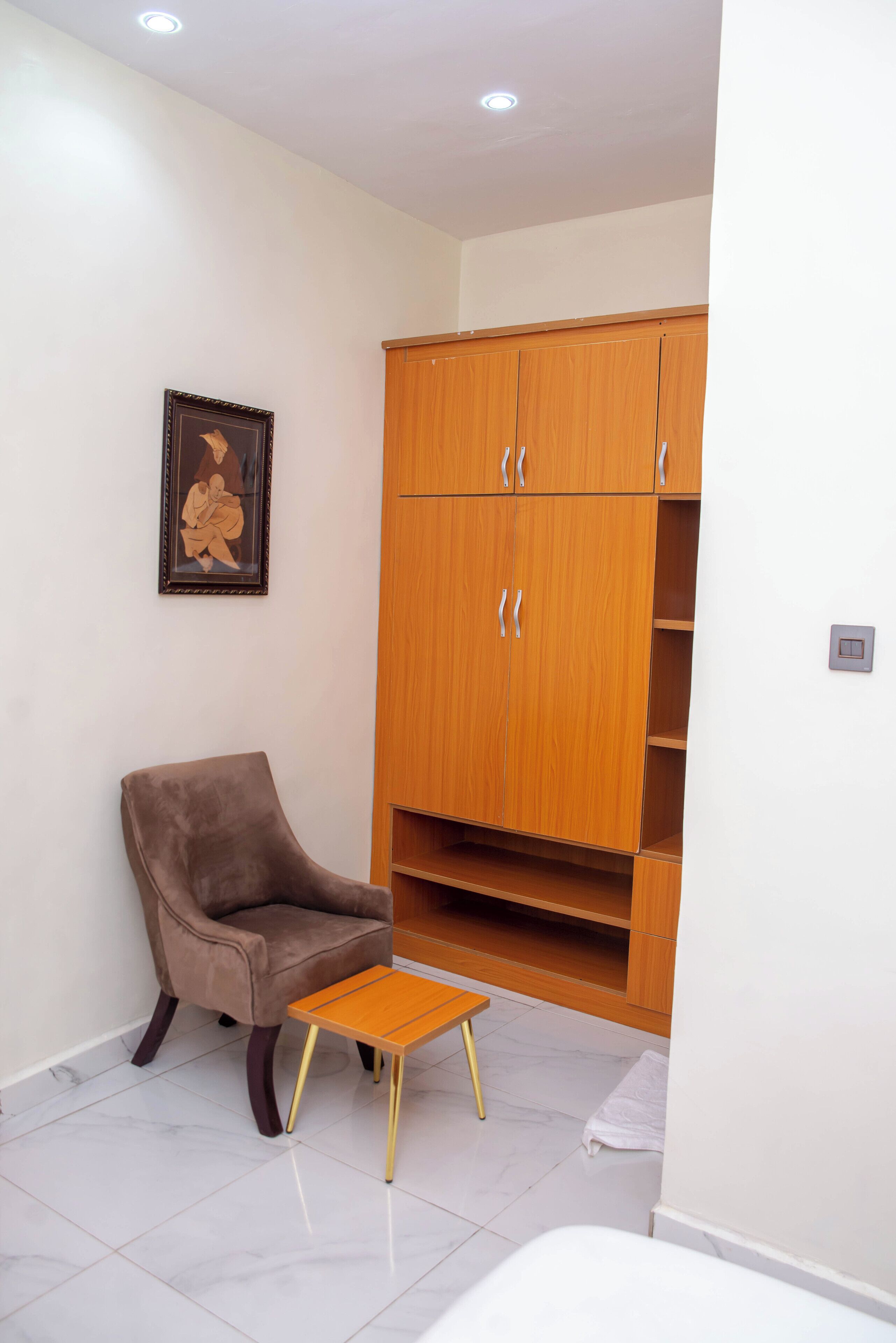 A room with a brown armchair, a small wooden table, and a wooden wardrobe with two doors and a shelf.