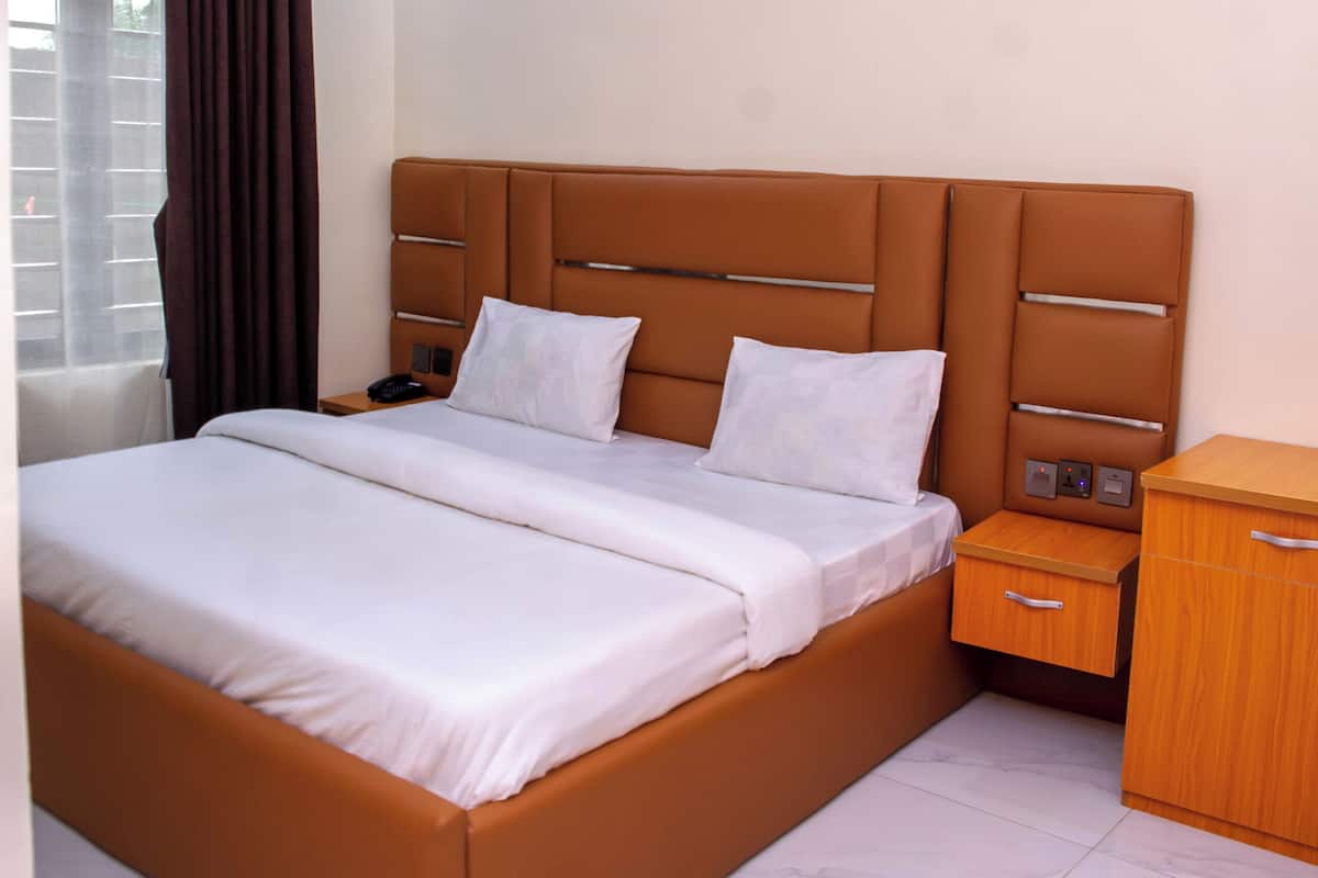A modern hotel room with a large bed, bedside tables, and a wooden nightstand.