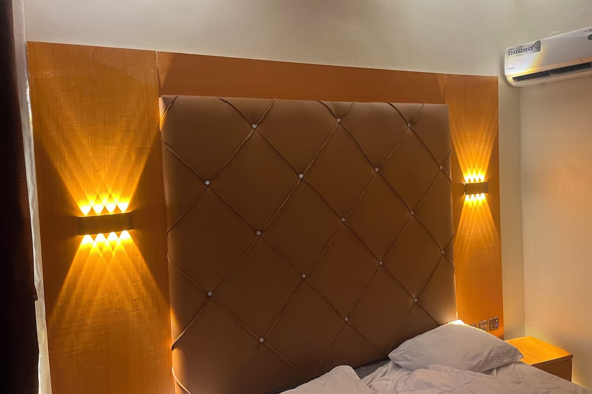 A bedroom with a tufted headboard, two wall-mounted lights, and an air conditioning unit.
