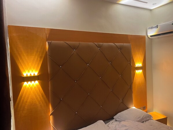 Un dormitorio con cabecera capitonada, dos lámparas de pared y un equipo de aire acondicionado.
