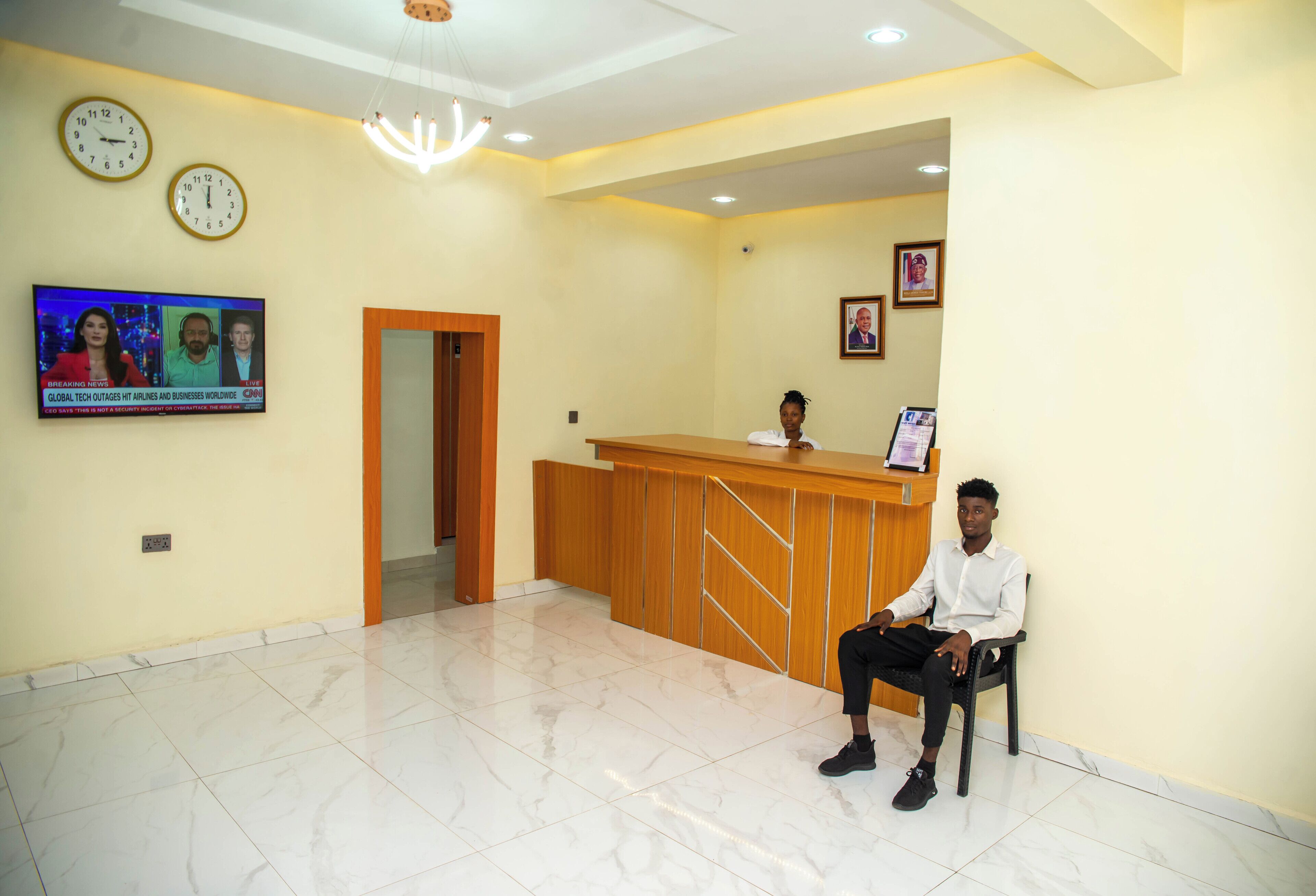 A reception area with a wooden desk, a television displaying news, and a tiled floor.