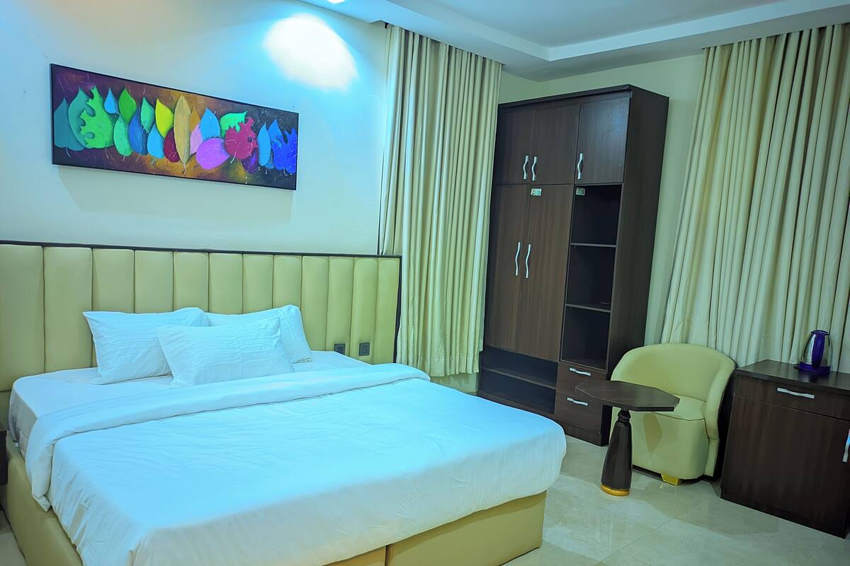 A hotel room with a large bed, a wardrobe, a desk, and a chair.