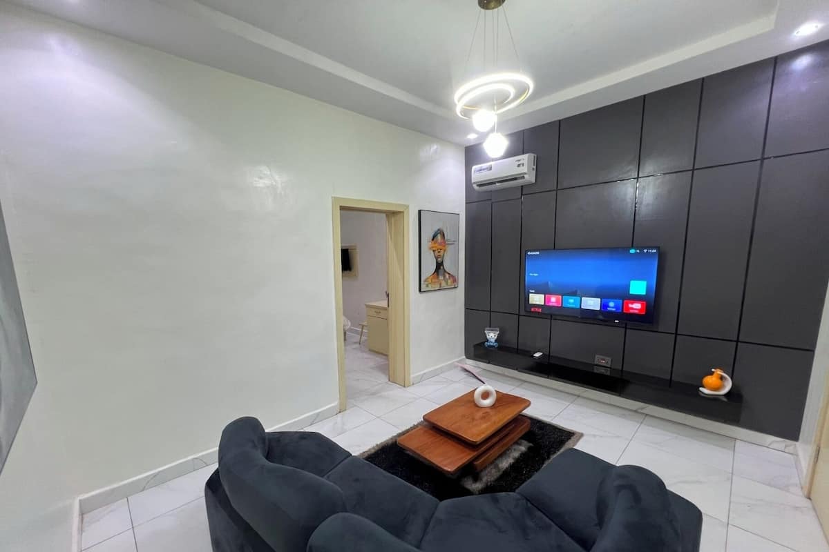 A modern living room with a flat-screen TV mounted on a dark wall, a sofa, a coffee table, and a small decorative item on the coffee table.