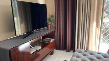 Een moderne woonkamer met een flatscreen televisie op een houten dressoir, een klein boekenrek en een comfortabele bank.