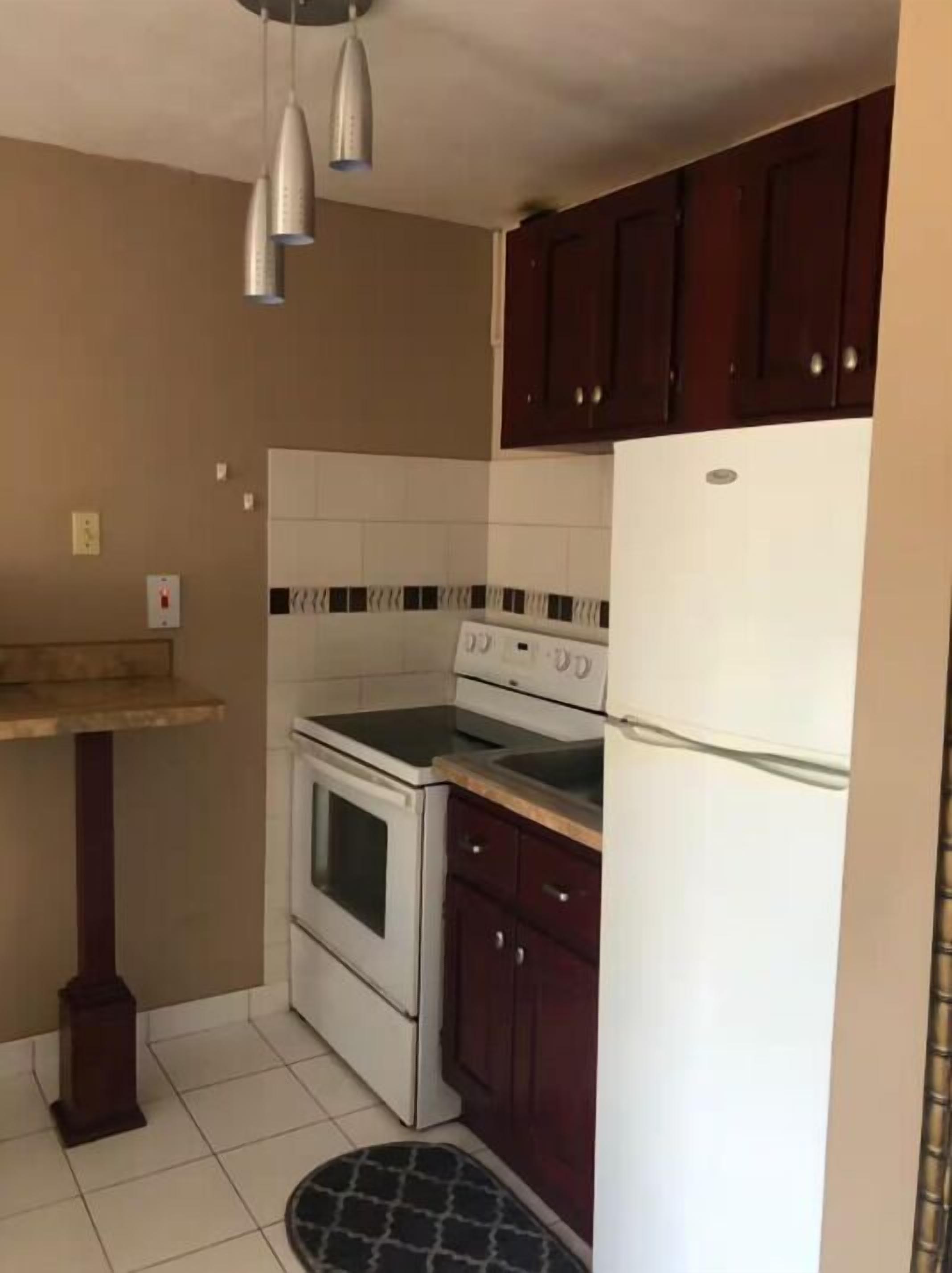 Eine Küche mit Herd, Backofen und Kühlschrank, Holzschränken und einer gefliesten Spritzschutzwand.